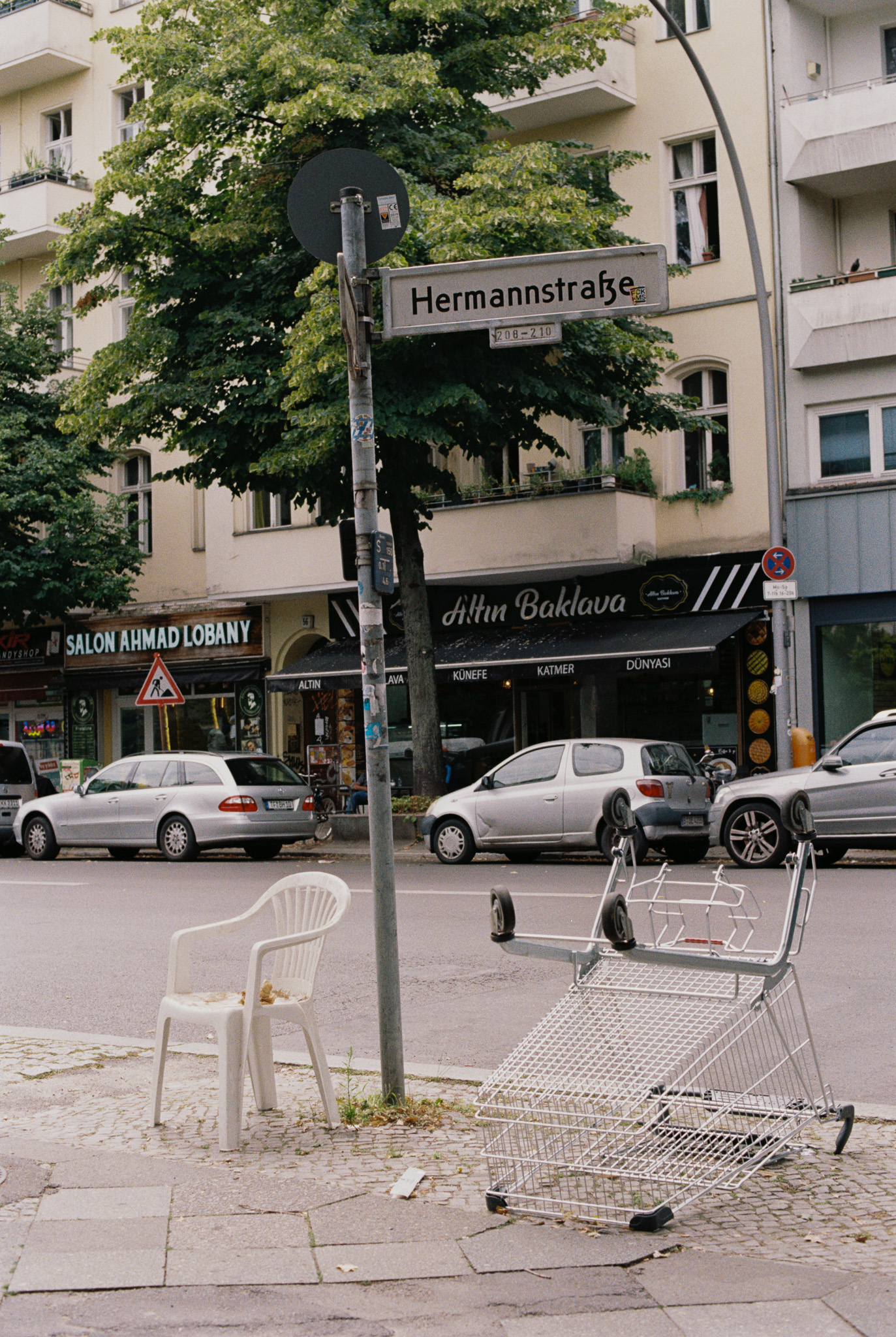 Abandoned shopping cart and plastic chair beneath the Hermannstraße sign, Neukölln