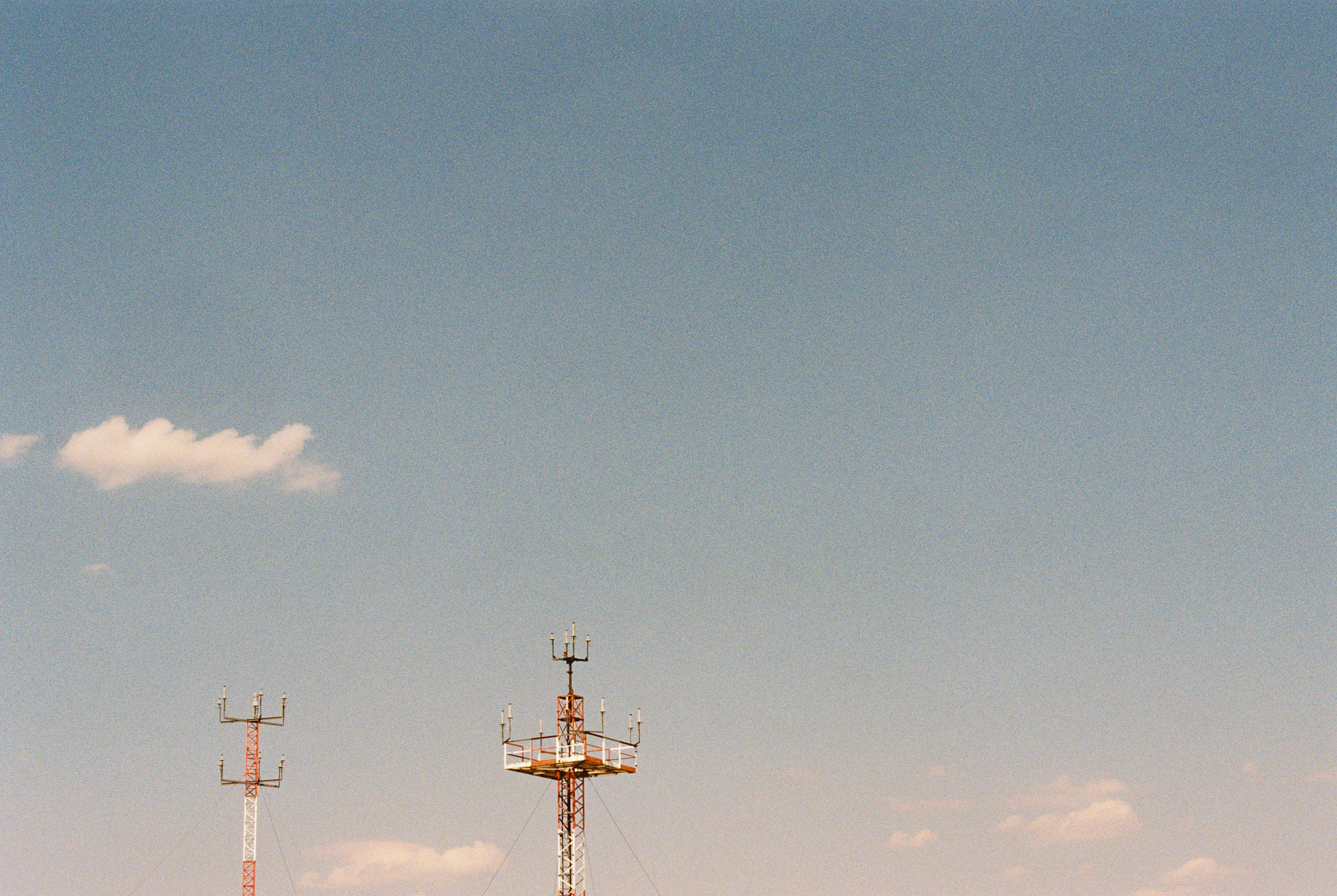 Two communication towers against a vast blue sky with a single cloud