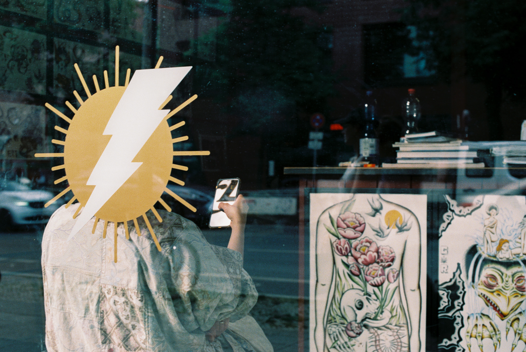 Reflection in a tattoo shop window with lightning bolt sun decal, Berlin