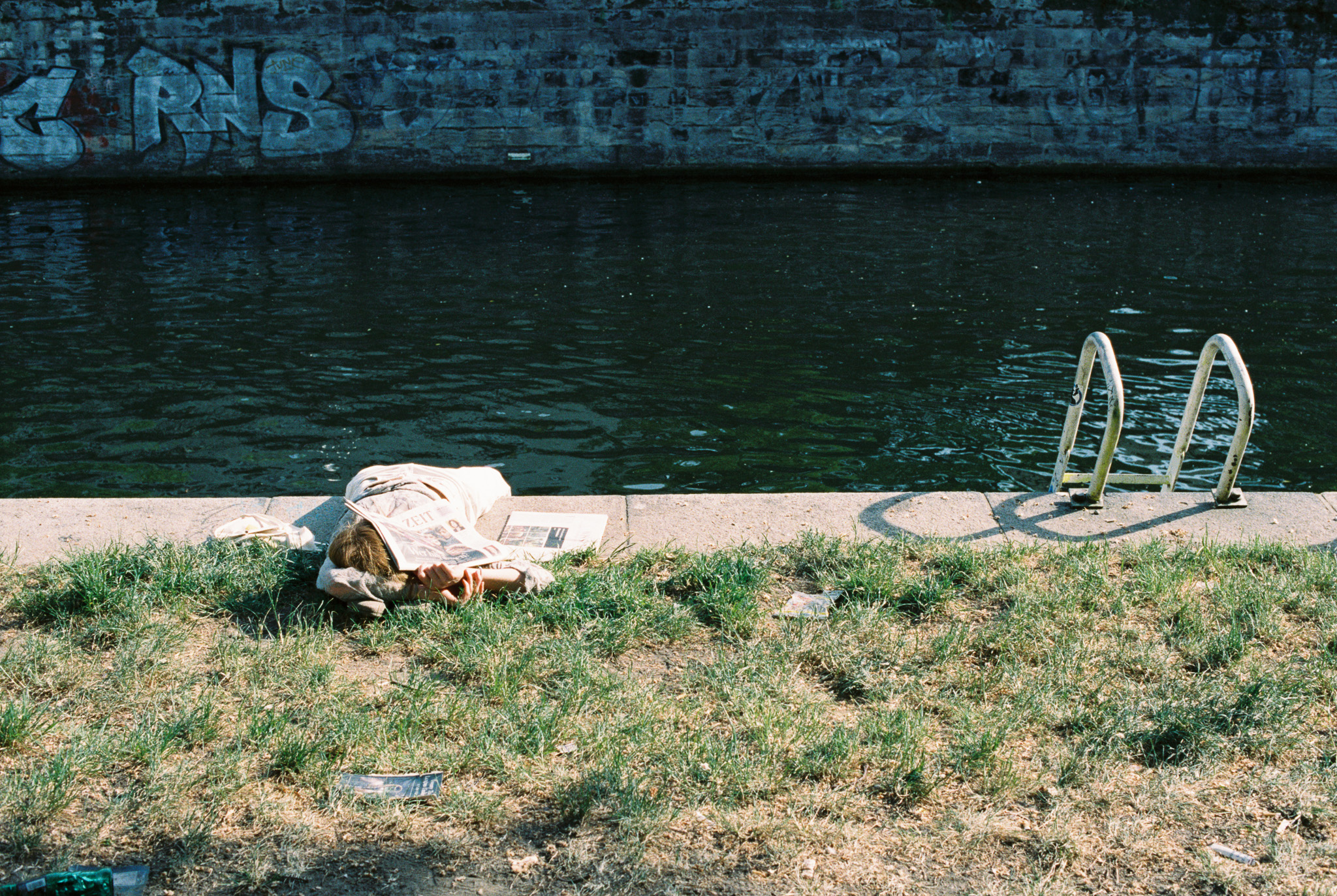 Newspaper and pool ladder at the edge of a canal with graffiti wall