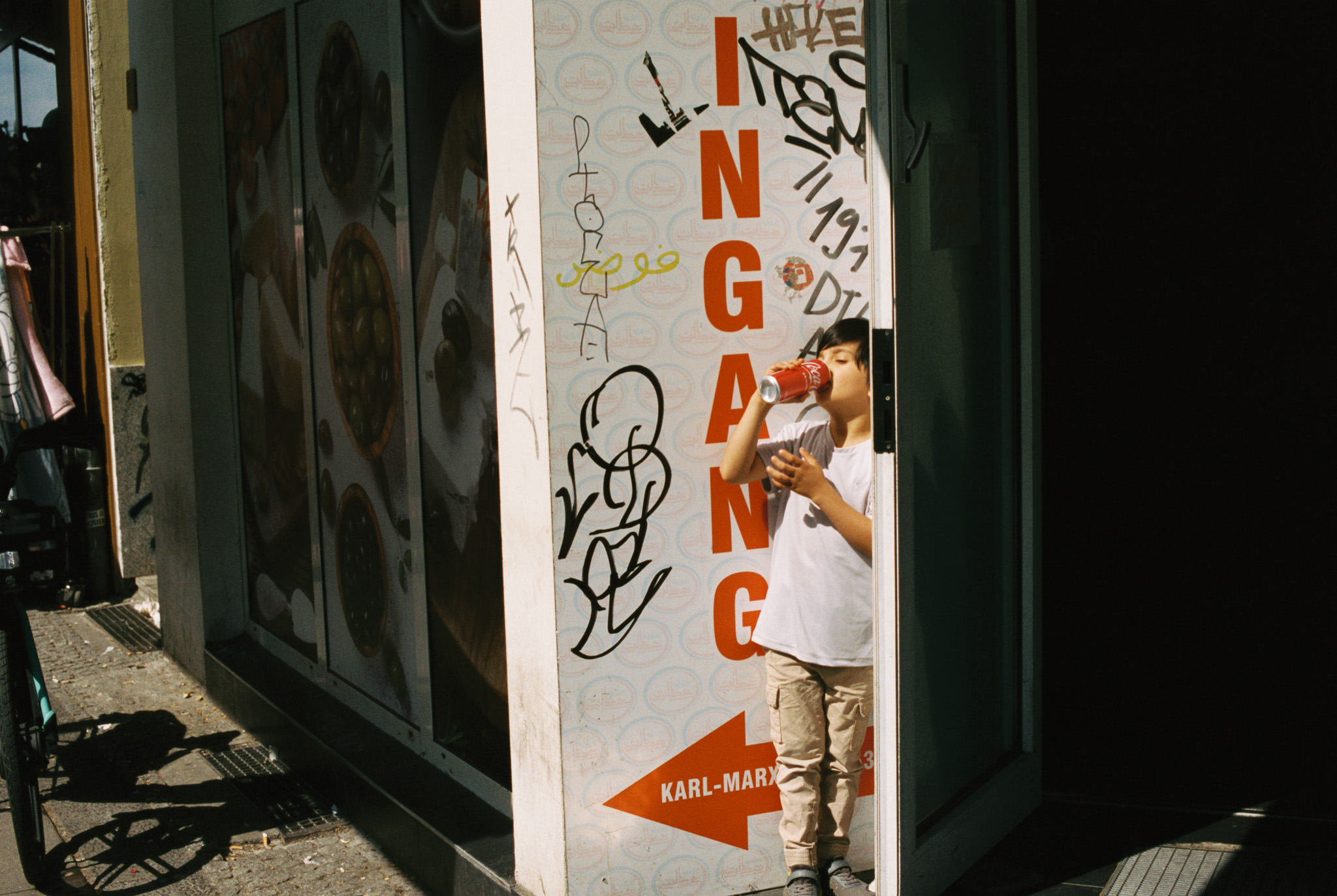 Child drinking from a can next to an entrance sign on Karl-Marx-Straße