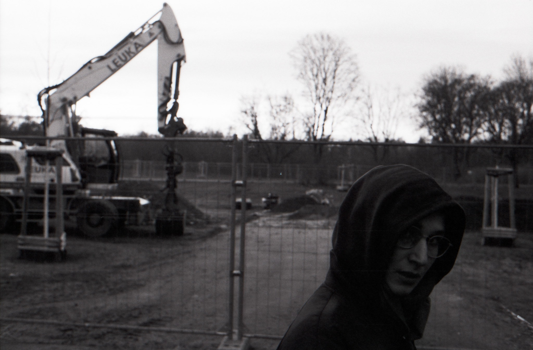 Person in a hoodie at a construction site with an excavator, black and white