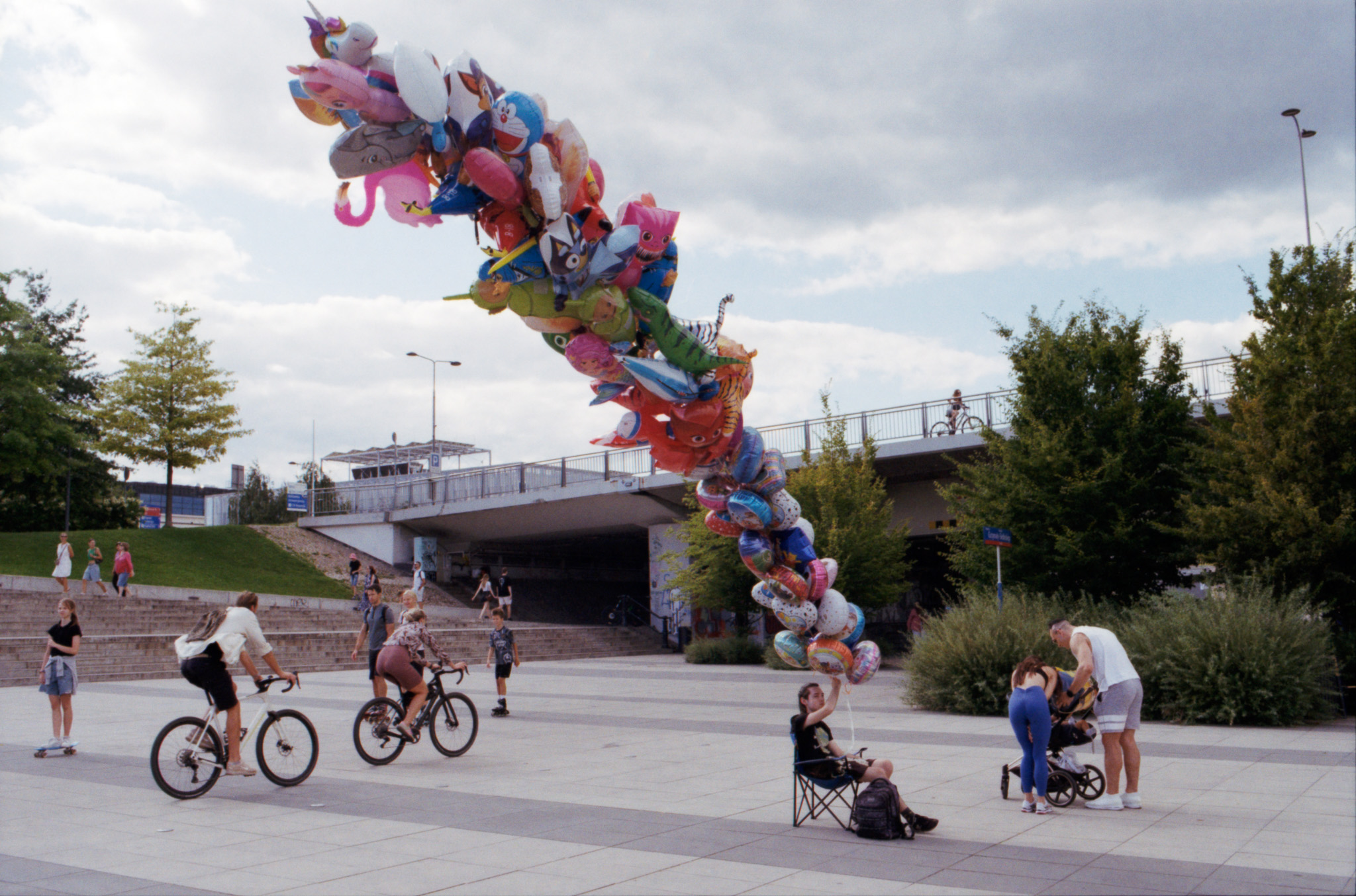 Balloon seller with colorful character balloons in a public square with cyclists