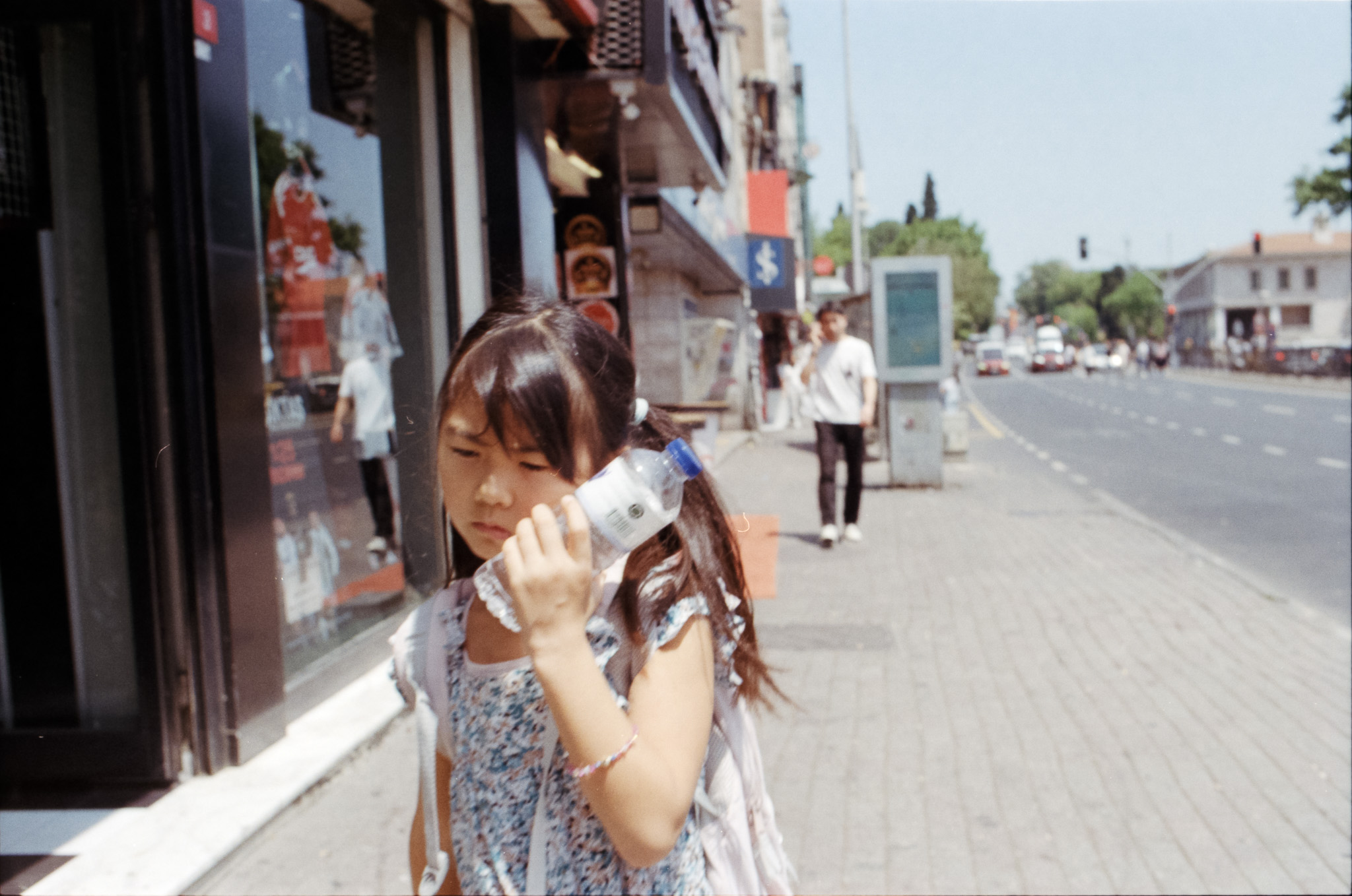 Girl holding a water bottle against her face on a sunny sidewalk
