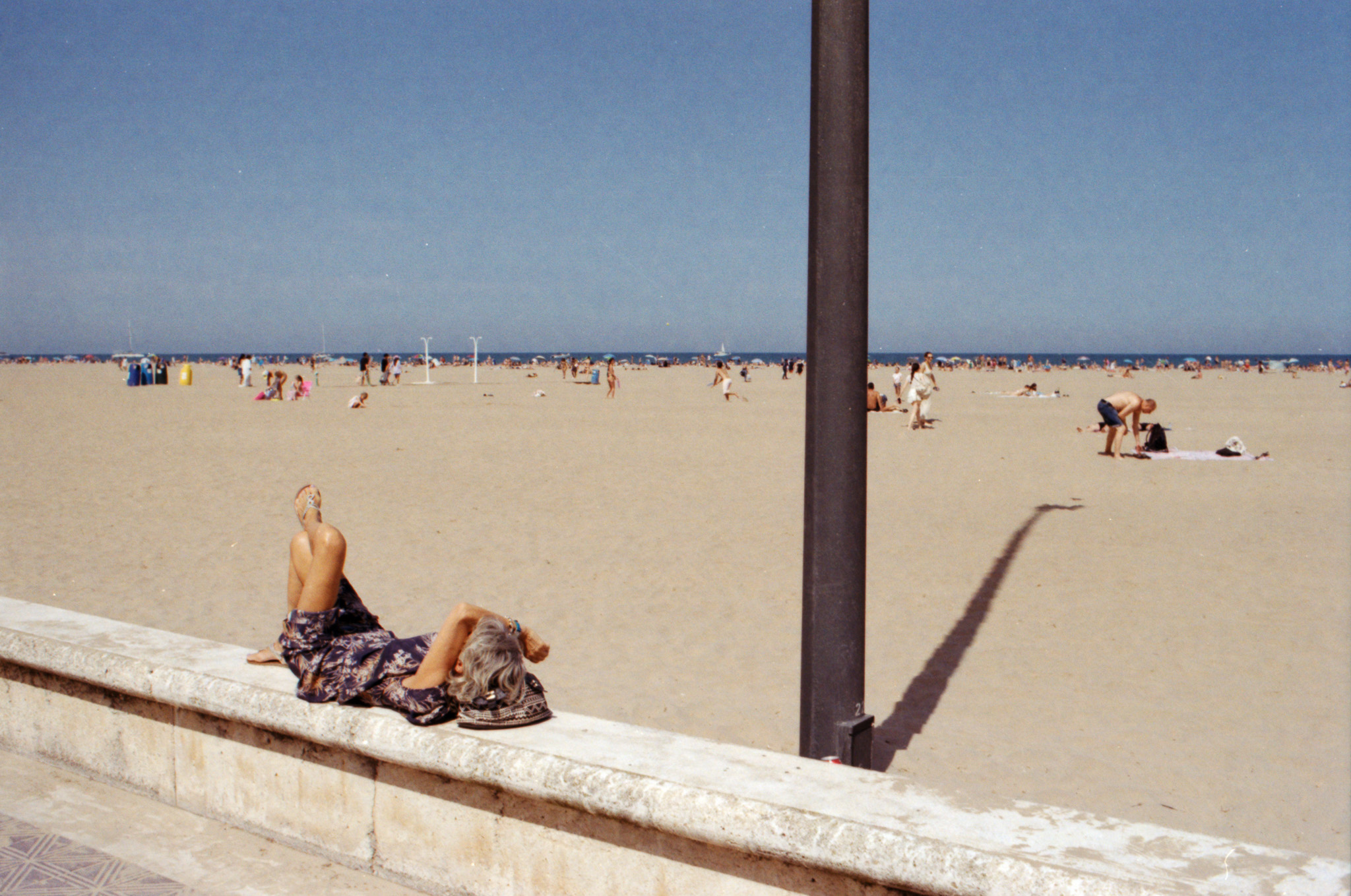 Woman reclining on a sea wall at a wide sandy beach, Valencia