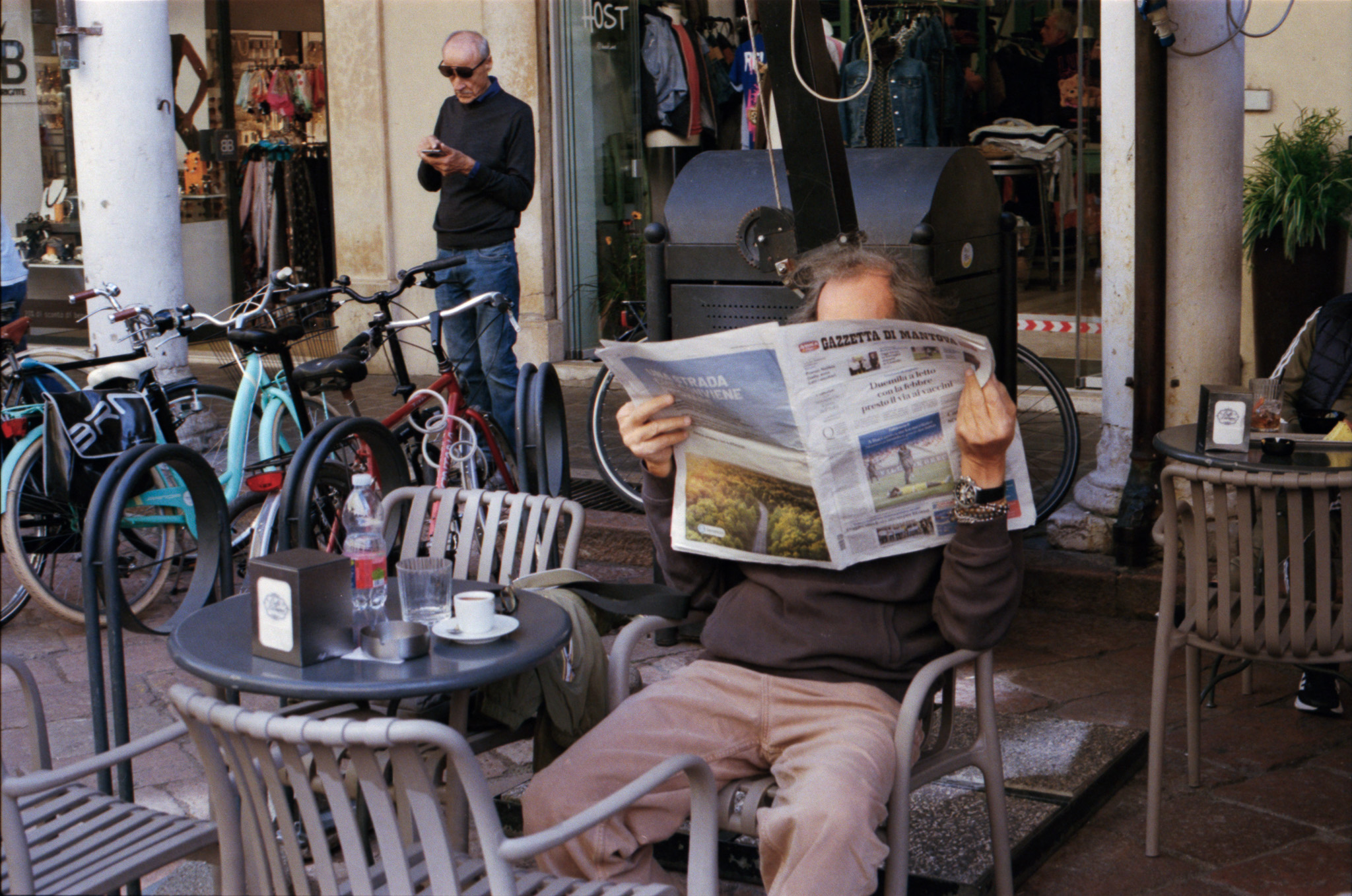 Man reading a newspaper at a cafe terrace with bicycles parked nearby, Italy