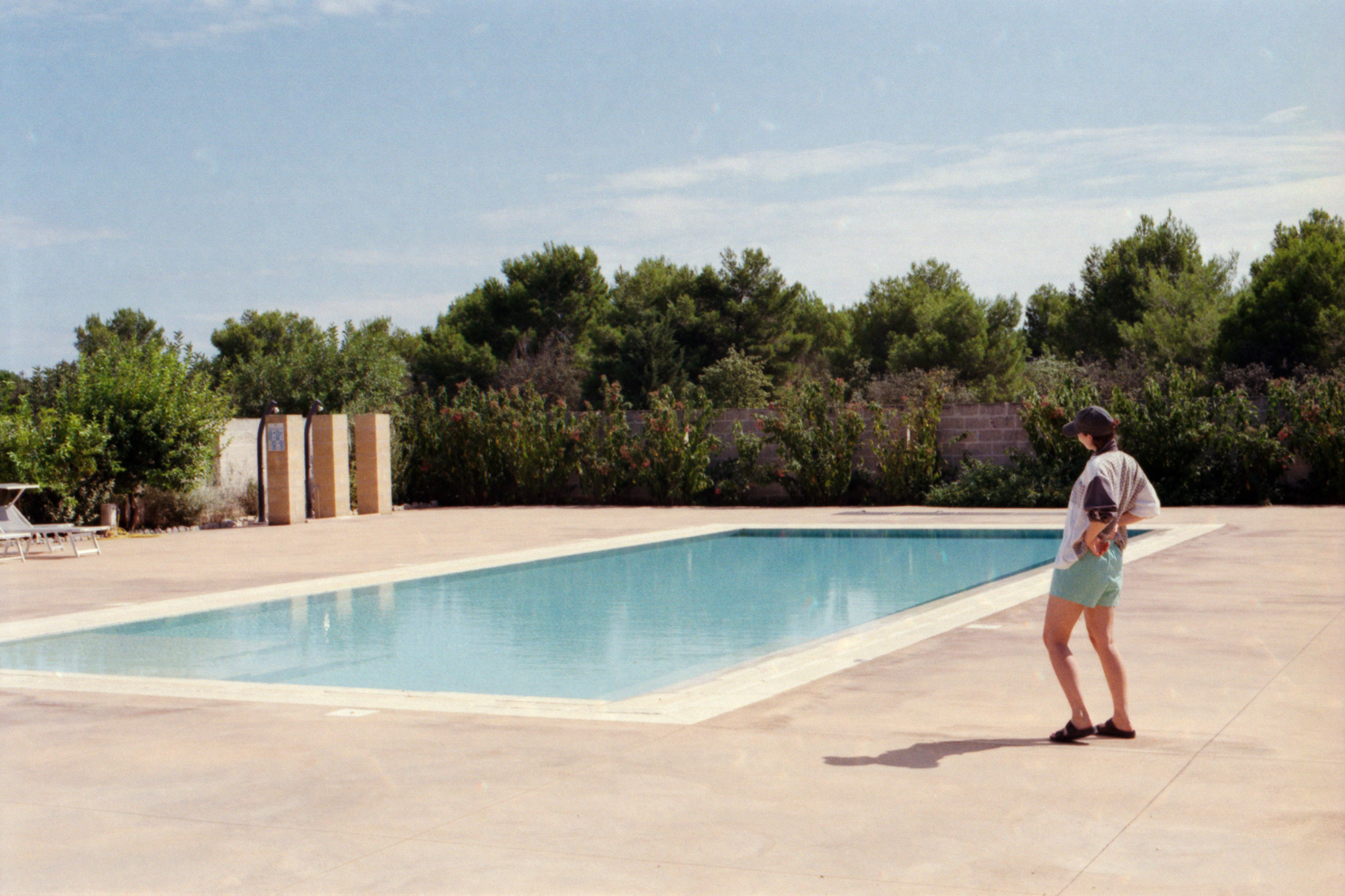 Person standing by an empty swimming pool surrounded by Mediterranean vegetation