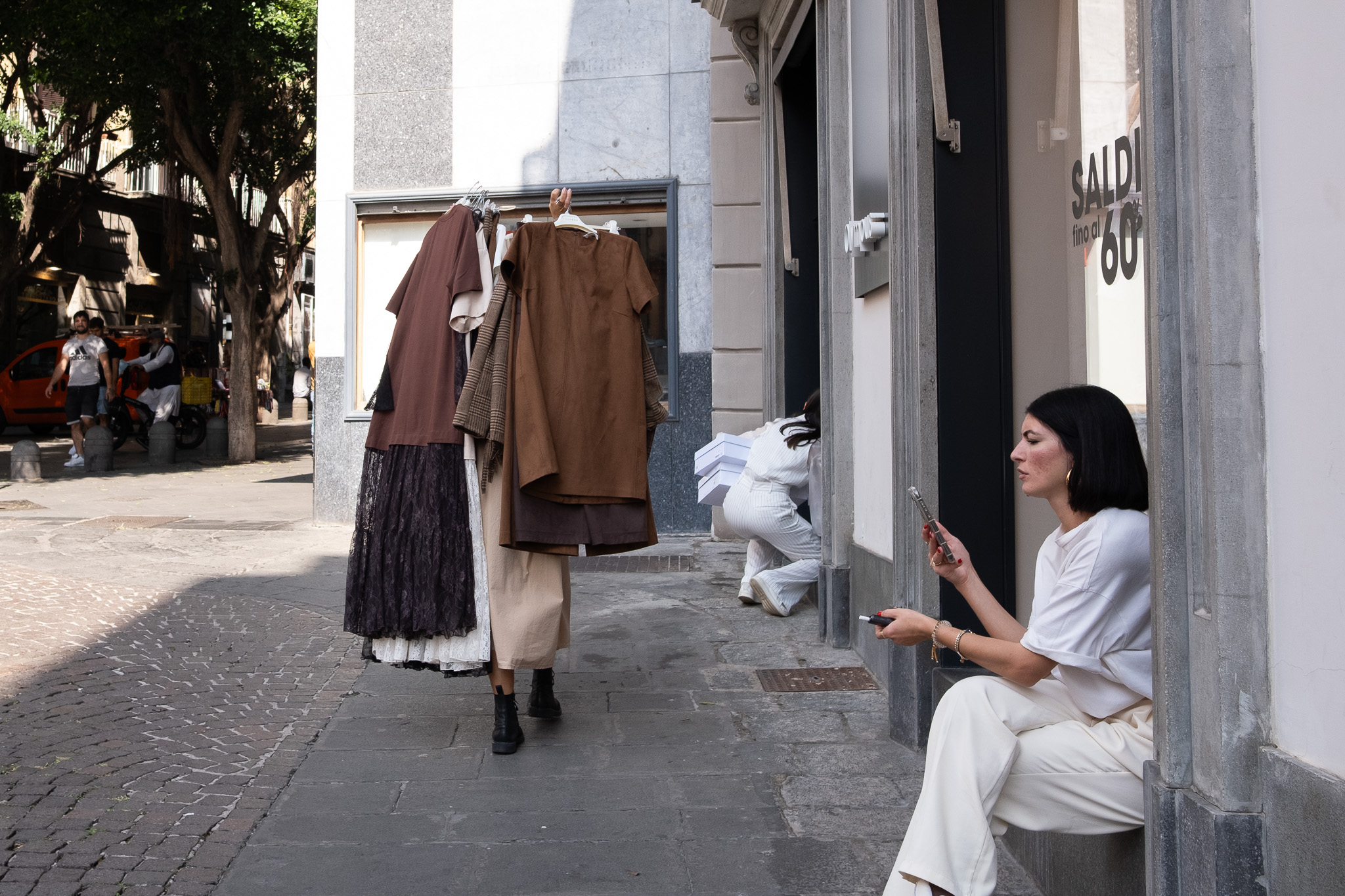 Woman sitting in a shop doorway on an Italian street with a clothes rack