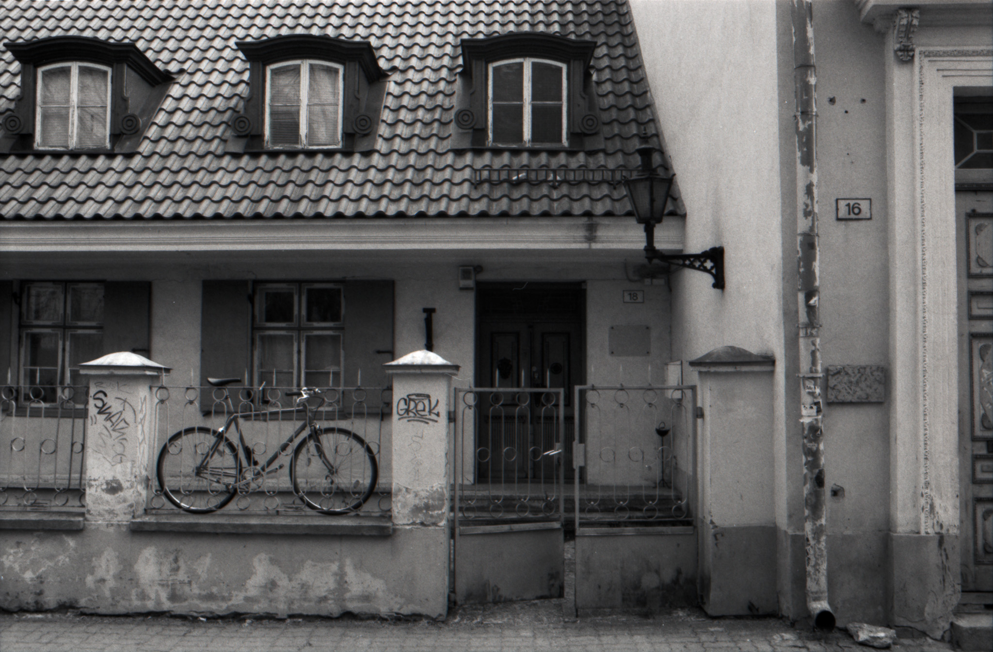 Bicycle leaning against an iron fence of an old house with dormer windows, black and white